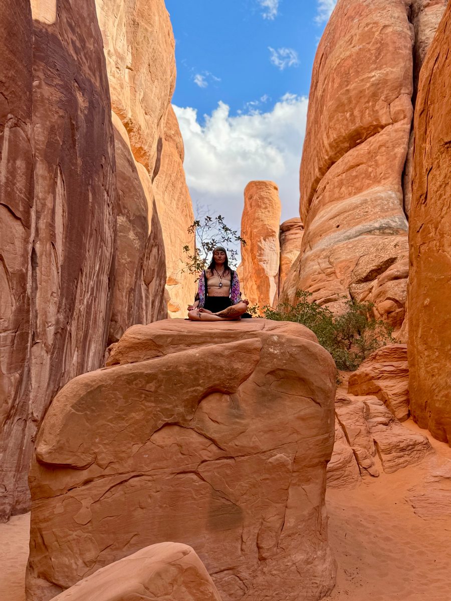 Sarah meditating on a sandstone boulder between towering red canyon walls