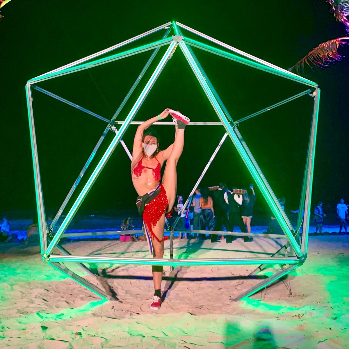 Sarah in a standing split inside a glowing geometric sculpture on the beach at night