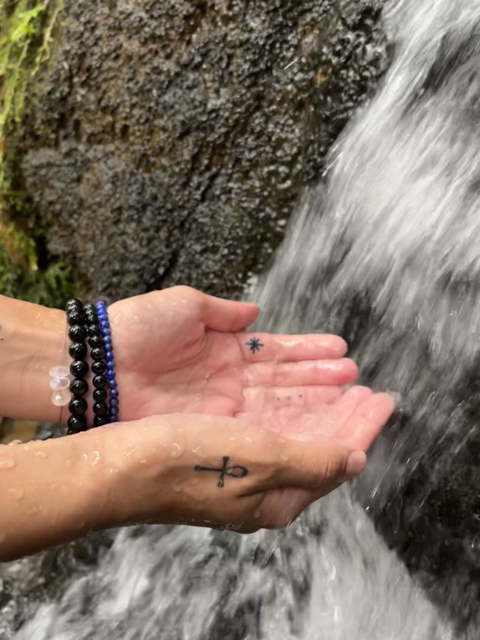Hands cupping water from a rainforest waterfall