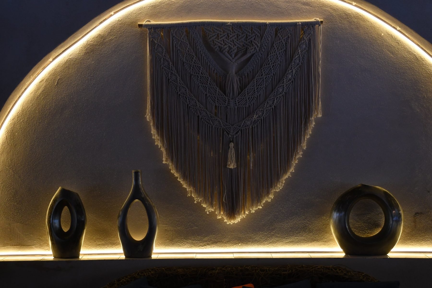 Macramé wall hanging and sculptural vases under a glowing arched wall